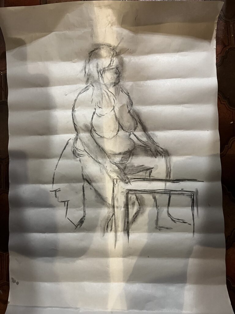 A photo of a charcoal drawing of a semi-nude model sitting on a chair, with one hand resting on a picture frame. The model has long hair.
