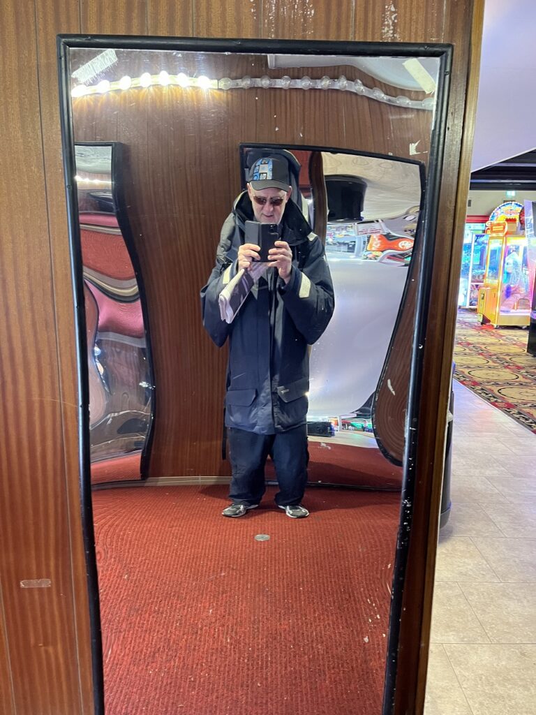 The author has taken a photo of himself in one of the exhibits in the "Hall of Mirrors". His legs have been shortened to about a third of their normal length, and his body lengthened by the same proportion. He wears a baseball cap, sunglasses and sailing jacket.